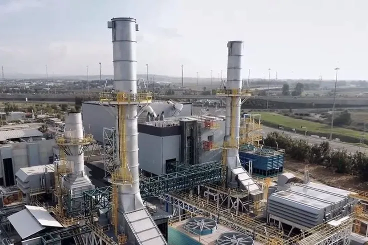 Aerial view of an industrial plant with tall chimneys, cooling fans, and surrounding infrastructure.