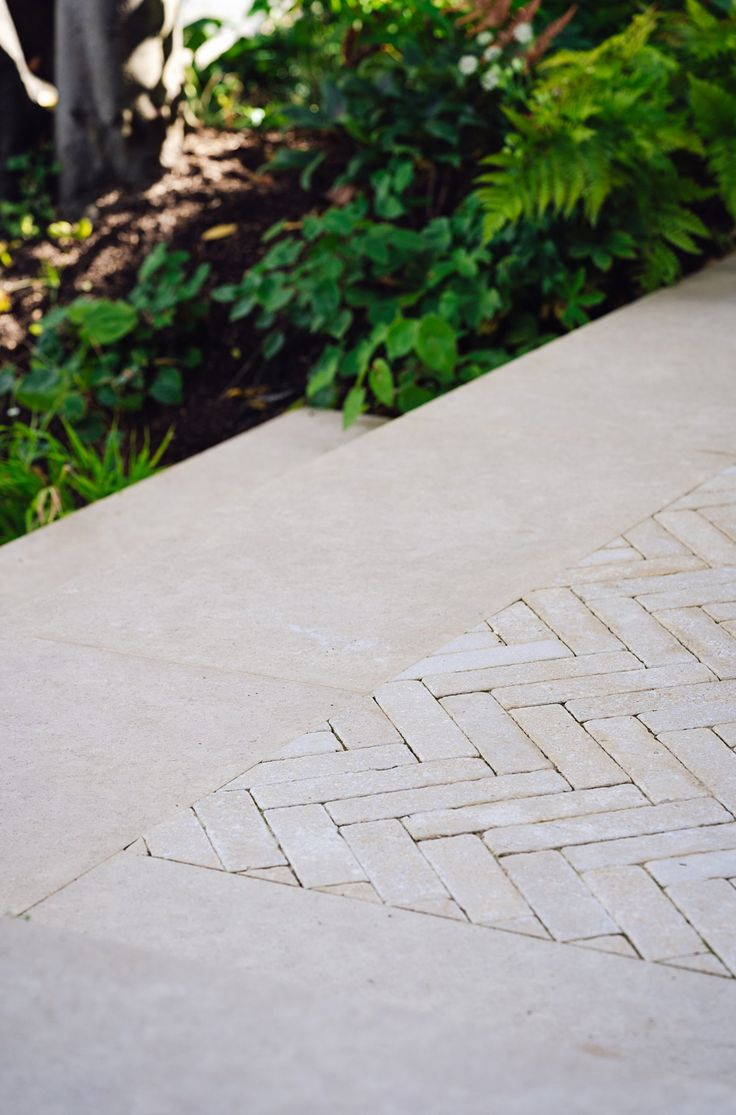 Modern desert backyard with a slate stepping stone path through gravel, flanked by large agaves, cacti, and succulents, with low teak wood bench seating and illuminated accent trees at dusk.
