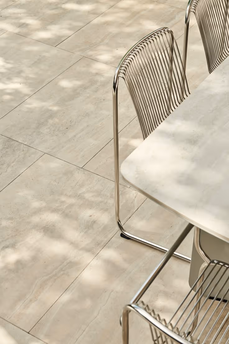 Tall tiered outdoor water feature with stacked stone column, cascading bowl tiers with LED lighting, surrounded by tropical bird of paradise, ferns, and red flowering plants against a wood fence at night.
