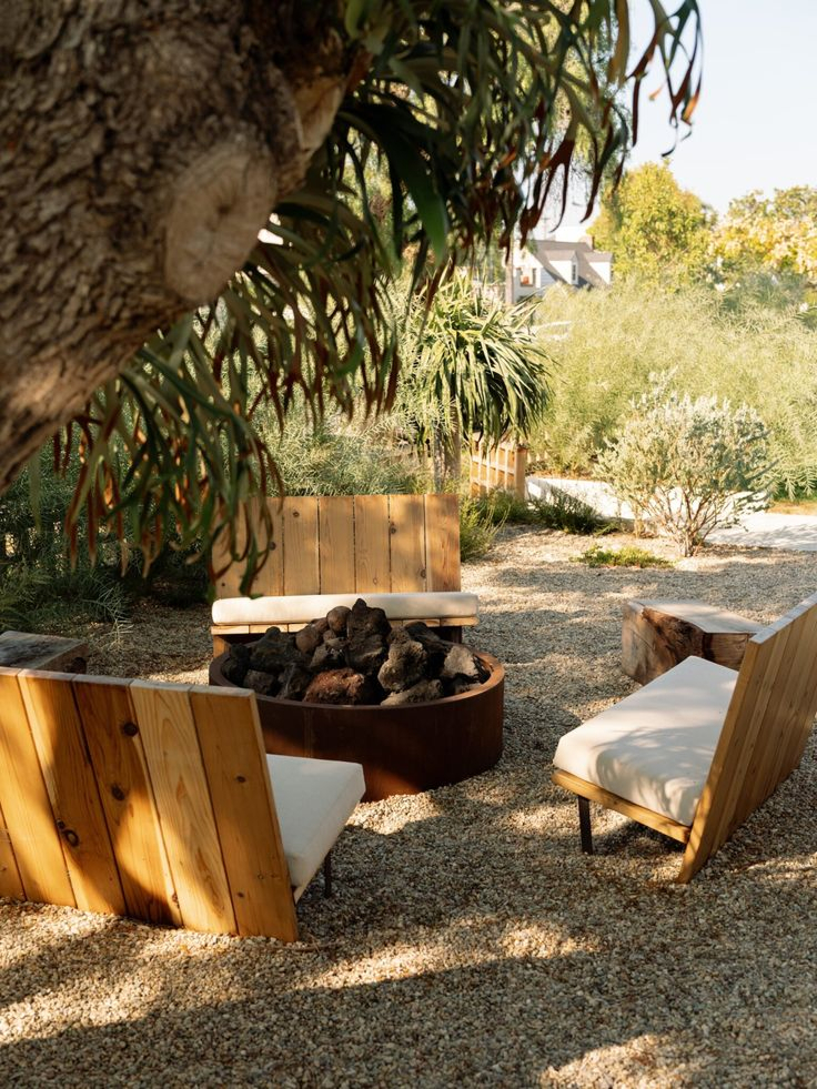 California desert-style backyard with fine decomposed granite ground cover, a round corten steel fire bowl, custom cedar lounge chairs with white cushions, and a surrounding mix of native shrubs, agave, and eucalyptus under dappled shade.