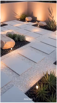 A dramatic nighttime garden with large white concrete pavers set in black lava rock, agave and succulents lit by low ground candles and warm uplighting against a white stucco wall.
