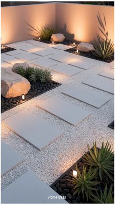 A dramatic nighttime garden with large white concrete pavers set in black lava rock, agave and succulents lit by low ground candles and warm uplighting against a white stucco wall.