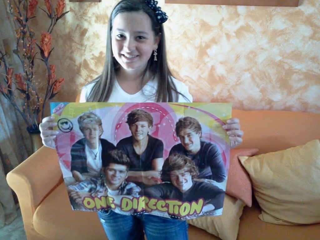 A young Federica smiling and holding a One Direction poster featuring all five members.