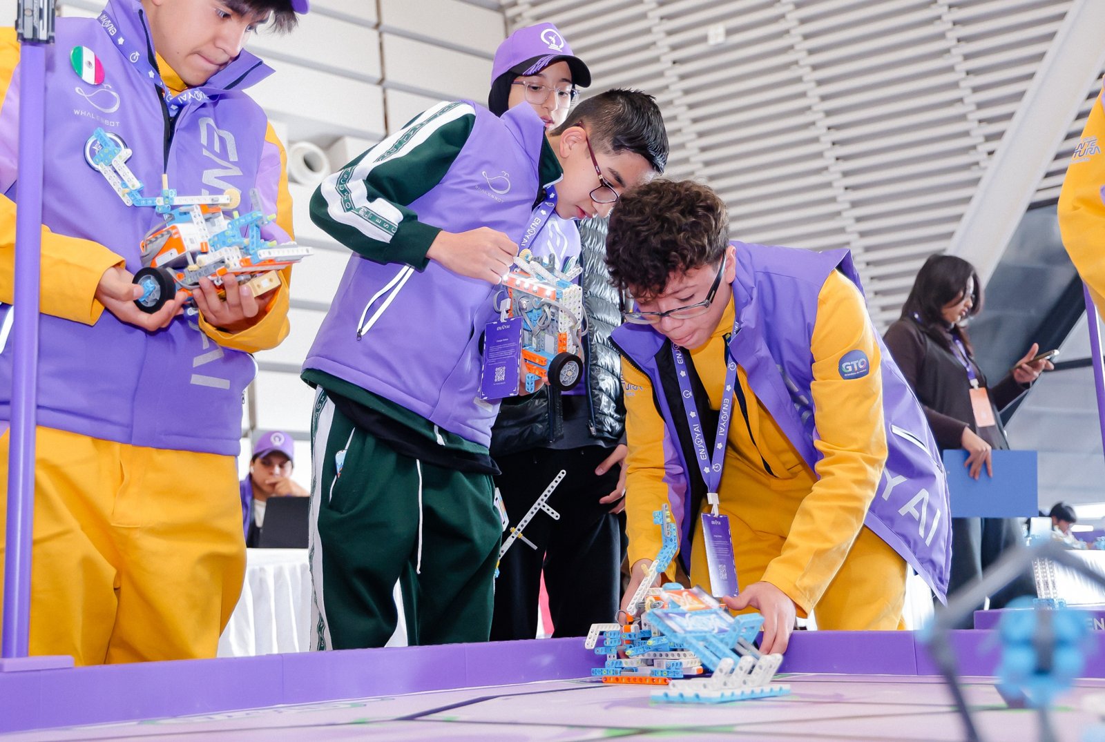 Alumnos con chaleco de EnjoyAI colocan su robot en la mesa de competencia