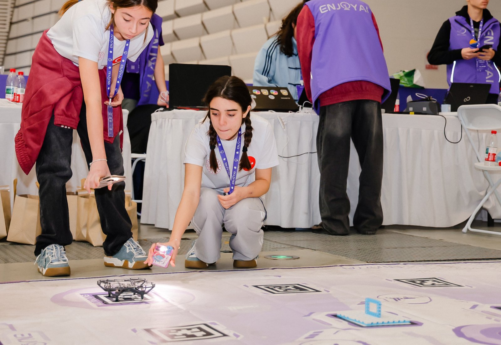Tres alumnos acomodan sus robots sobre una mesa de competencia de EnjoyAI