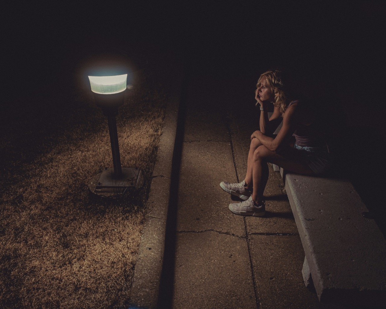 une femme seule dans l'obscurité qui attends devant une lampe allumée