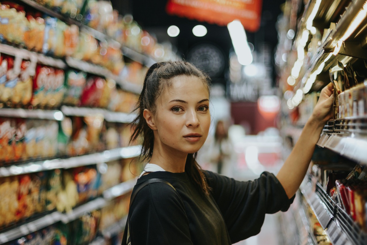 Femme au supermarché qui choisis ses aliments et regarde la caméra. Illium l'application de l'amour pour les célibataires et les couples.