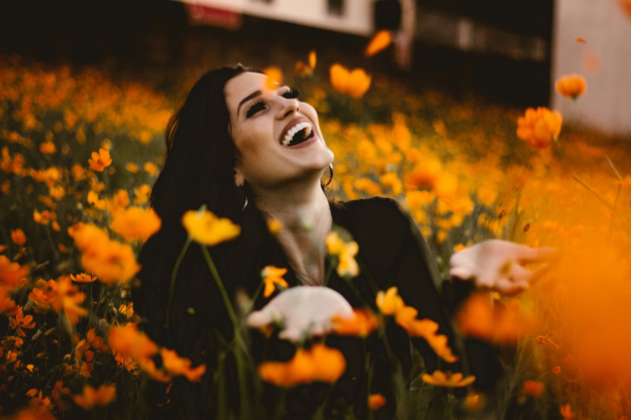 femme heureuse et libérée dans un champs de fleurs oranges. Illium l'application de l'amour pour les célibataires et les couples.