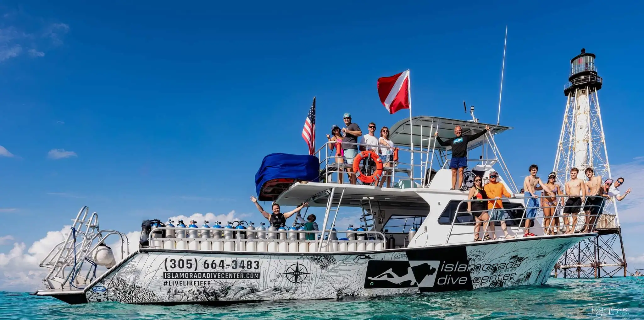 Group of people on Islamorada Dive Center dive boat in clear blue water near Alligator lighthouse under a bright blue sky.