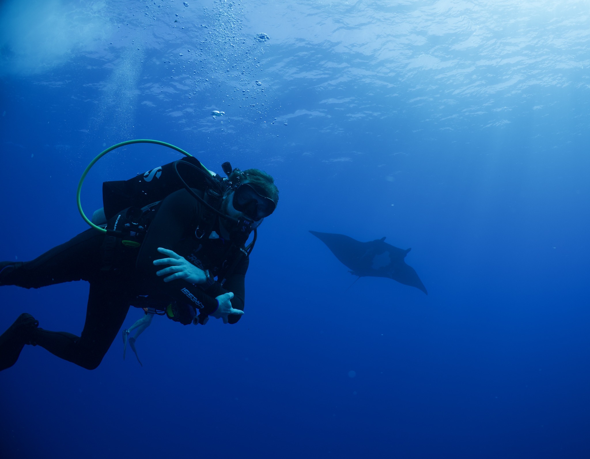 Scuba diver underwater near a manta ray in deep blue ocean.