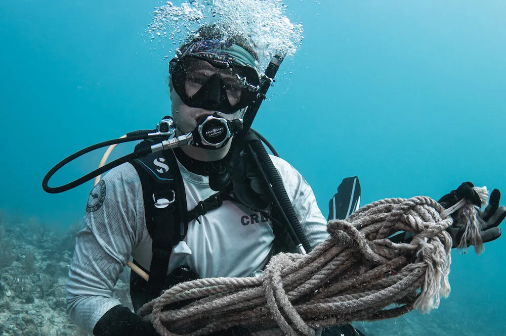 Scuba diver underwater holding a coiled rope while exhaling bubbles.