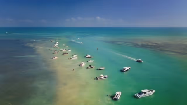 Boats anchored along a sandbar in clear turquoise ocean under a blue sky.