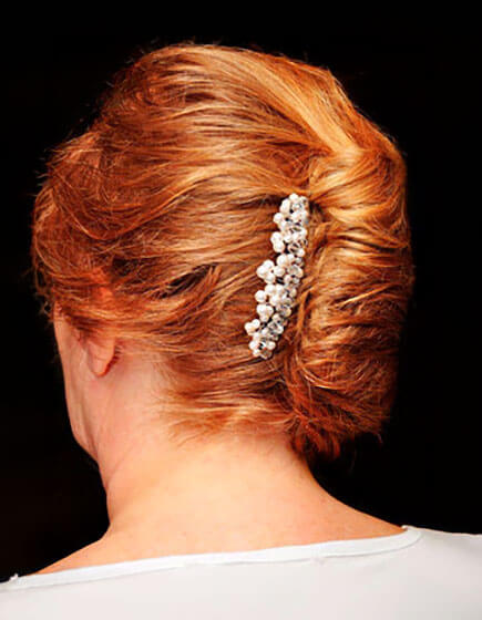 Back view of a person with red hair styled in an elegant updo secured with a decorative hair clip adorned with small white flowers.