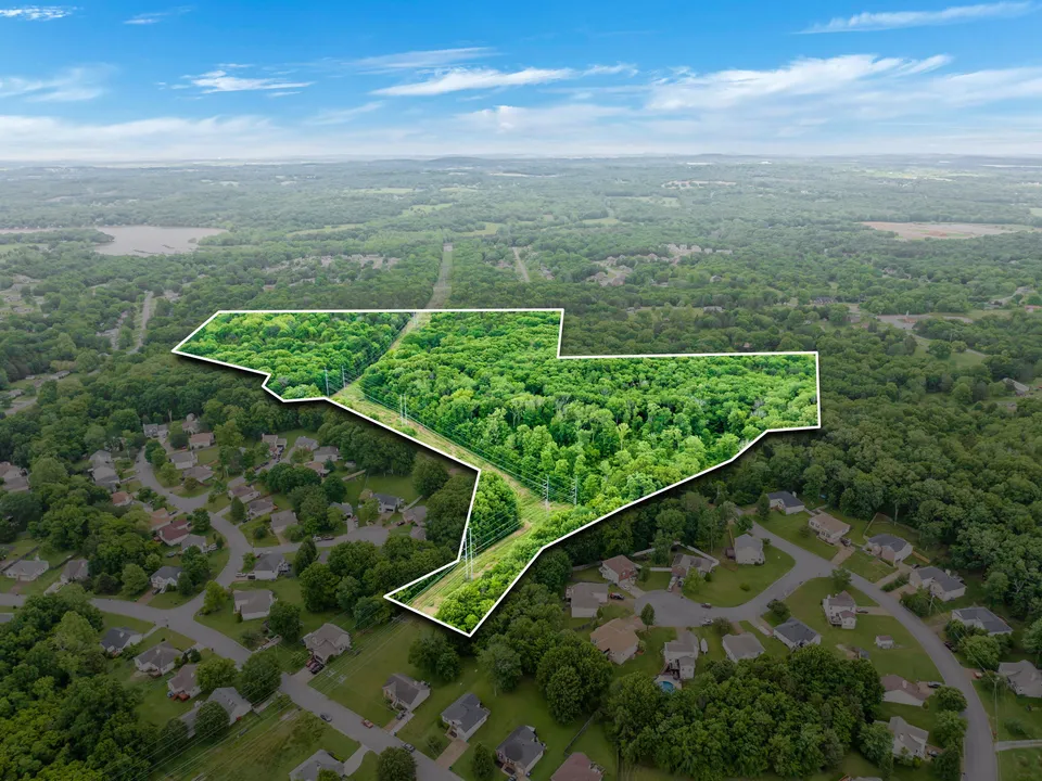 Aerial view of a suburban area with a highlighted wooded plot of land outlined in white.