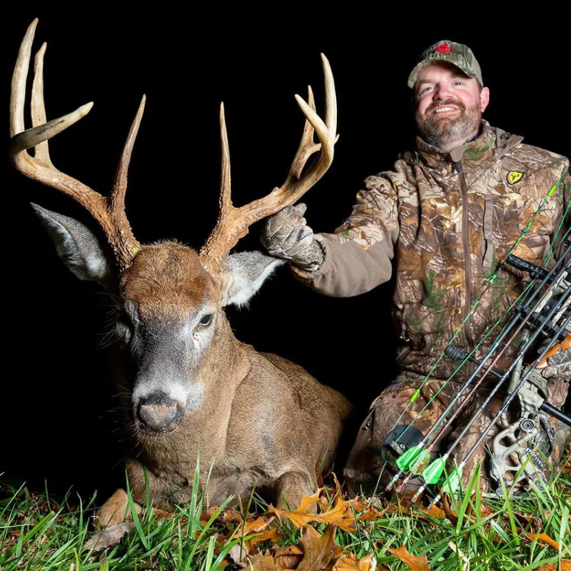 Paul Morrison in camouflage gear kneeling beside large buck deer with big antlers at night.