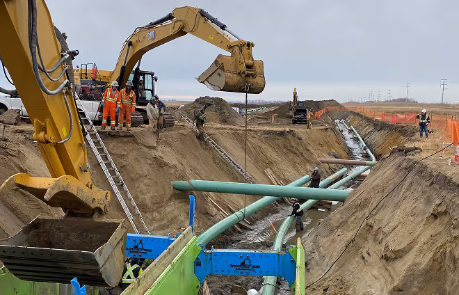 A pipeline installation in a large trench, with two excavators working nearby.