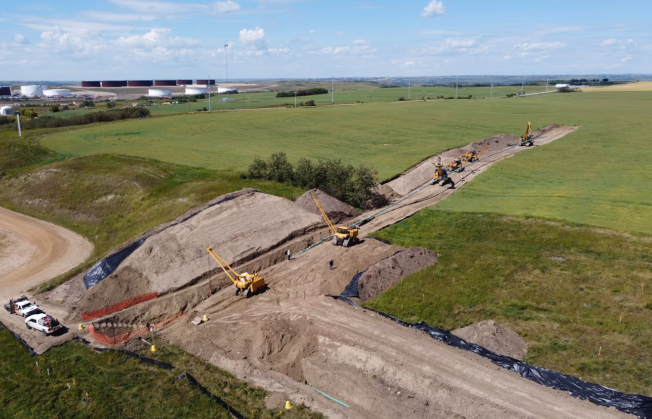 A drone shot of a pipeline installation in an empty field, featuring several pieces of heavy equipment.