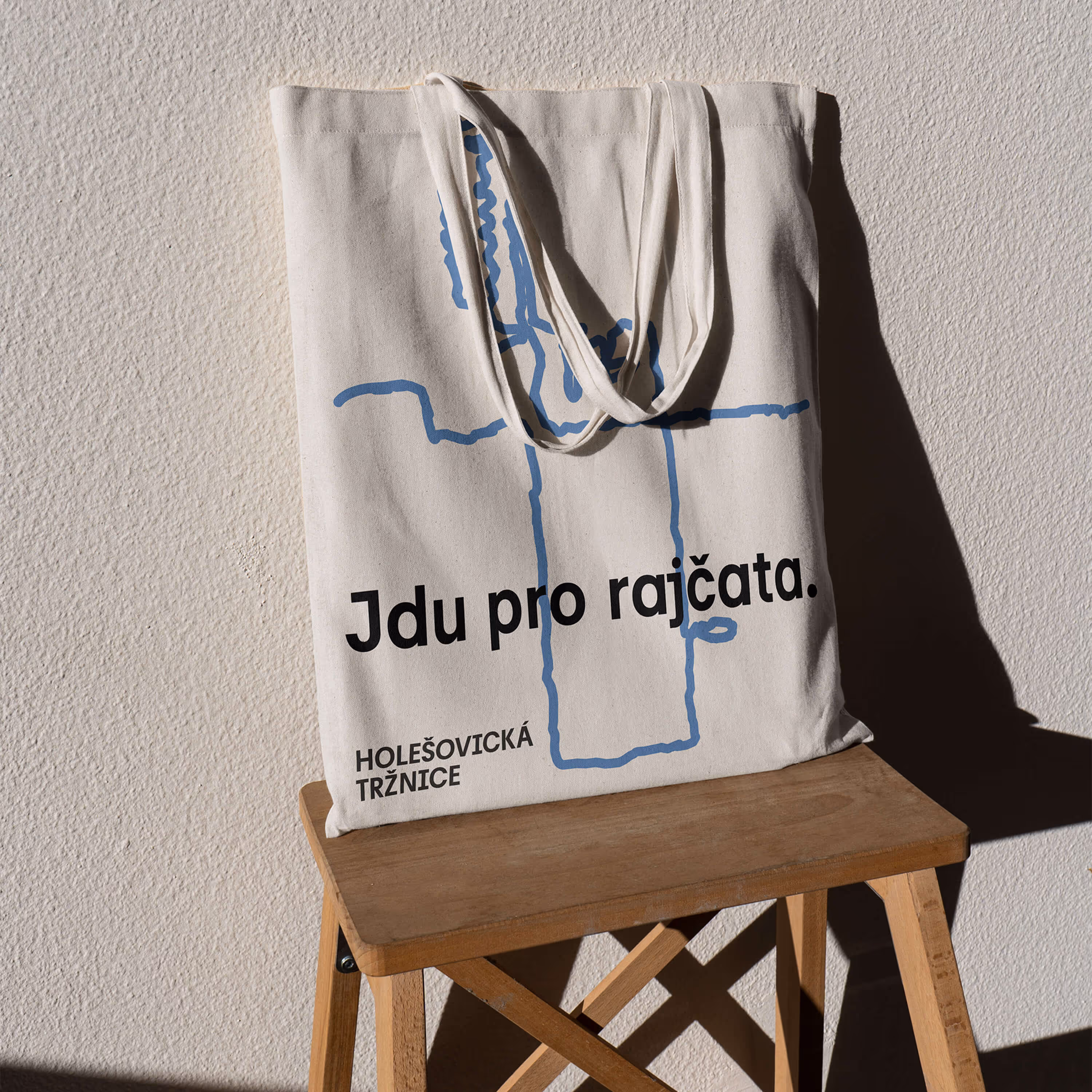 Bavlněná taška s nápisem Jdu pro rajčata a modrým abstraktním potiskem na dřevěné židli.
