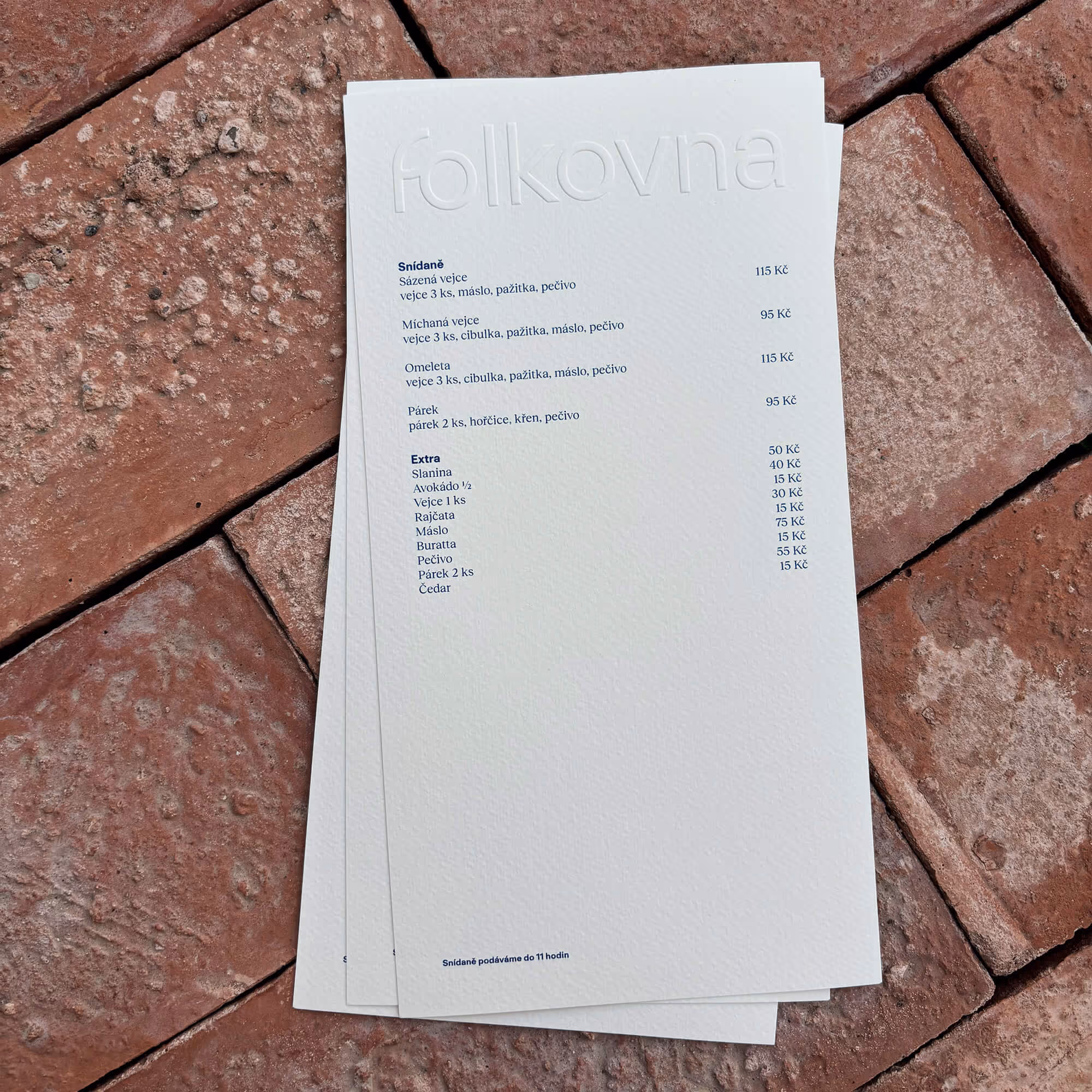 Menu s českými snídaněmi jako míchaná vejce, omeleta a párky na červených dlaždicích.