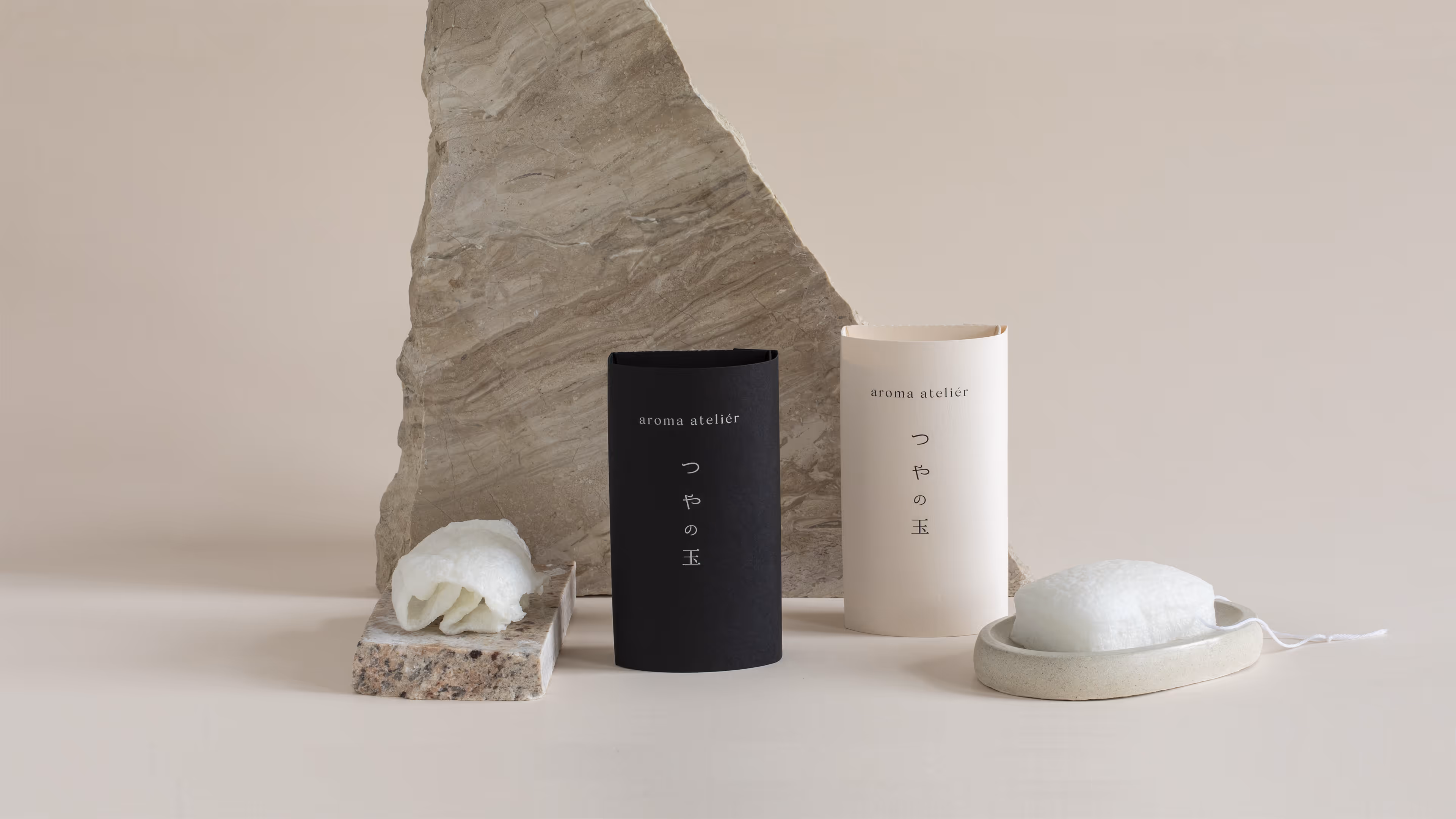 Černý a bílý obal aroma ateliéru vedle texturovaných kamenů a bílého přírodního produktu.