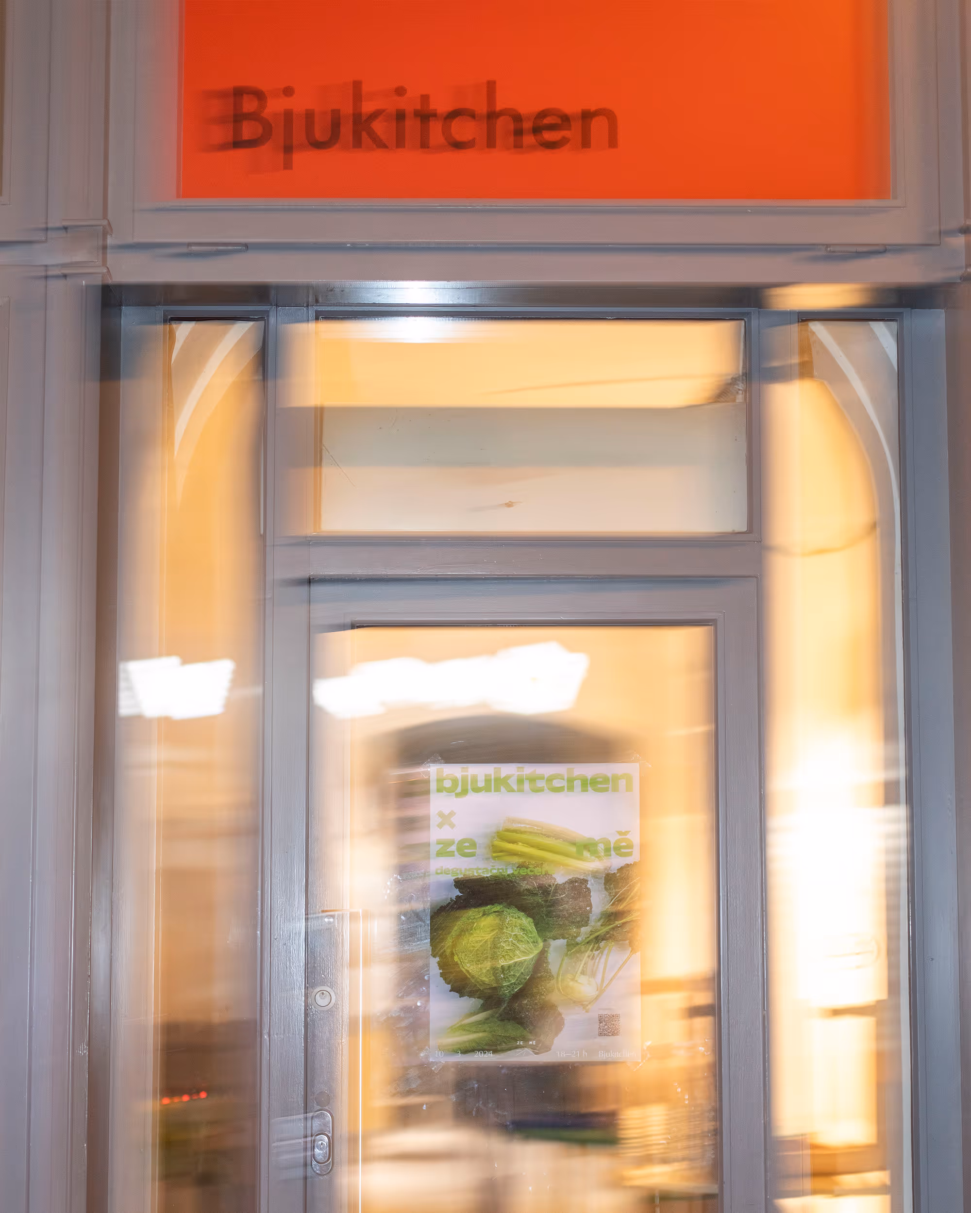 Rozmazaný pohled na dveře s nápisem Bjukitchen a plakátem s zeleninou.