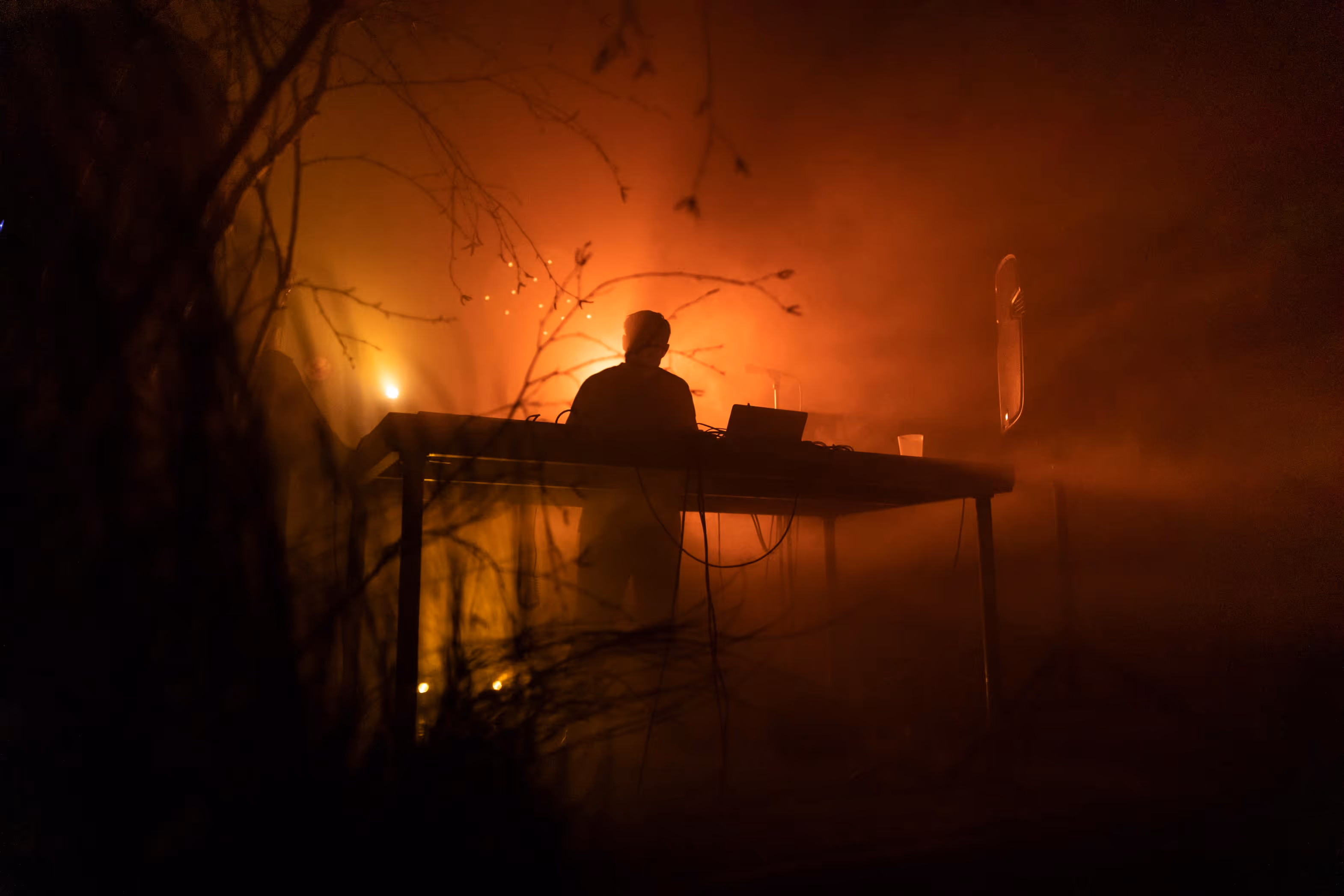 Osamělý DJ za stolem se světlem a kouřem v pozadí na tmavé večerní akci.
