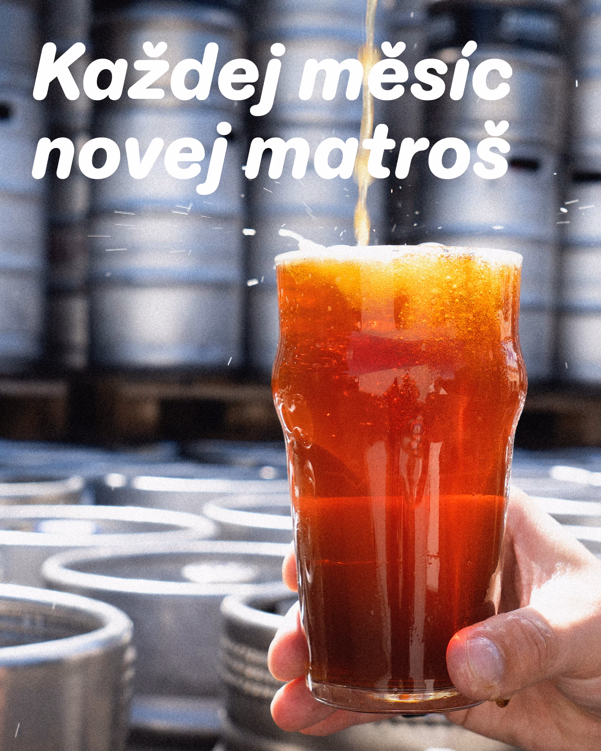 Ruka drží sklenici tmavého piva s pěnou před pozadím kovových soudků v pivovaru.