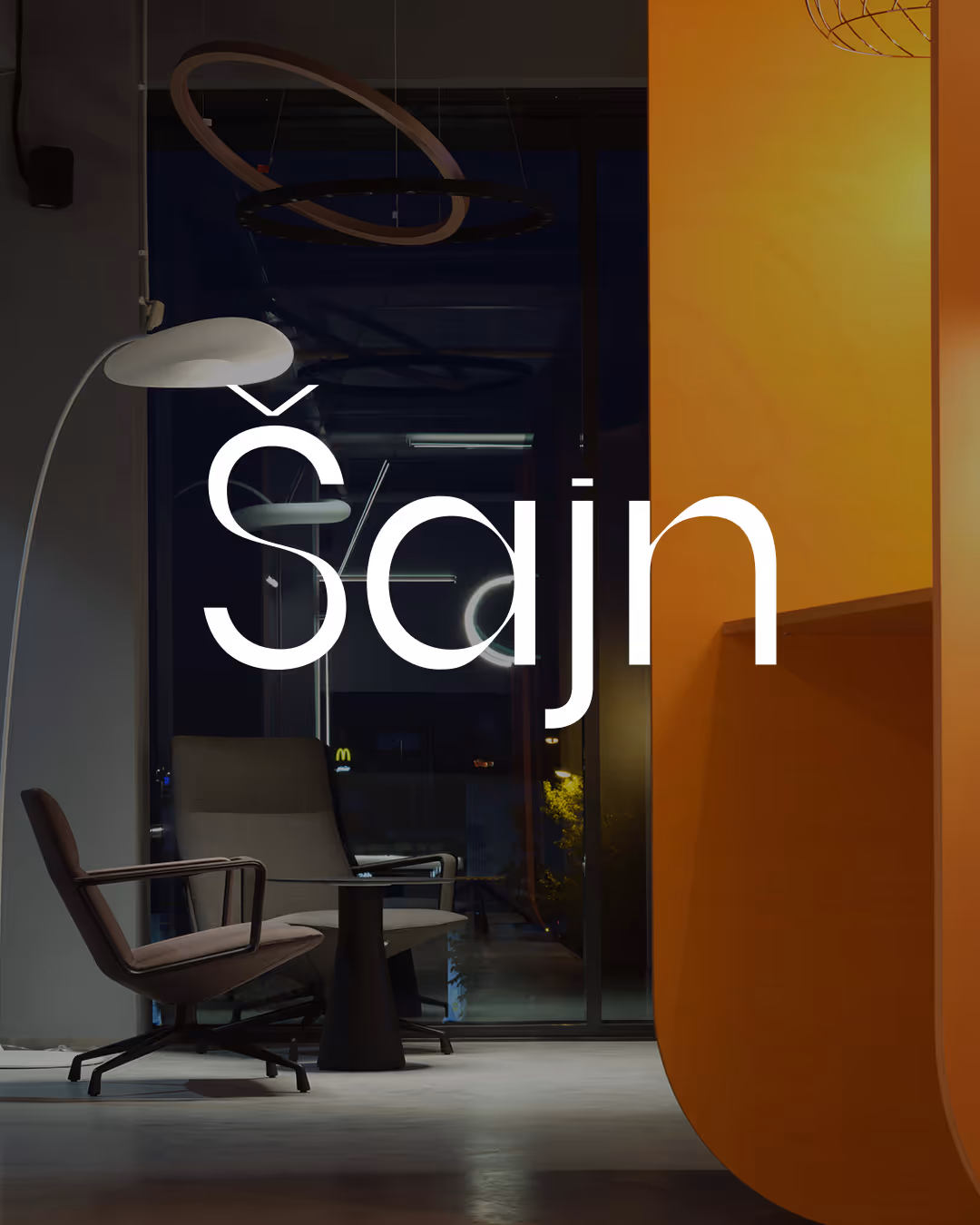 Modern indoor scene with two gray chairs, a round black table, floor lamp, and large orange wall.