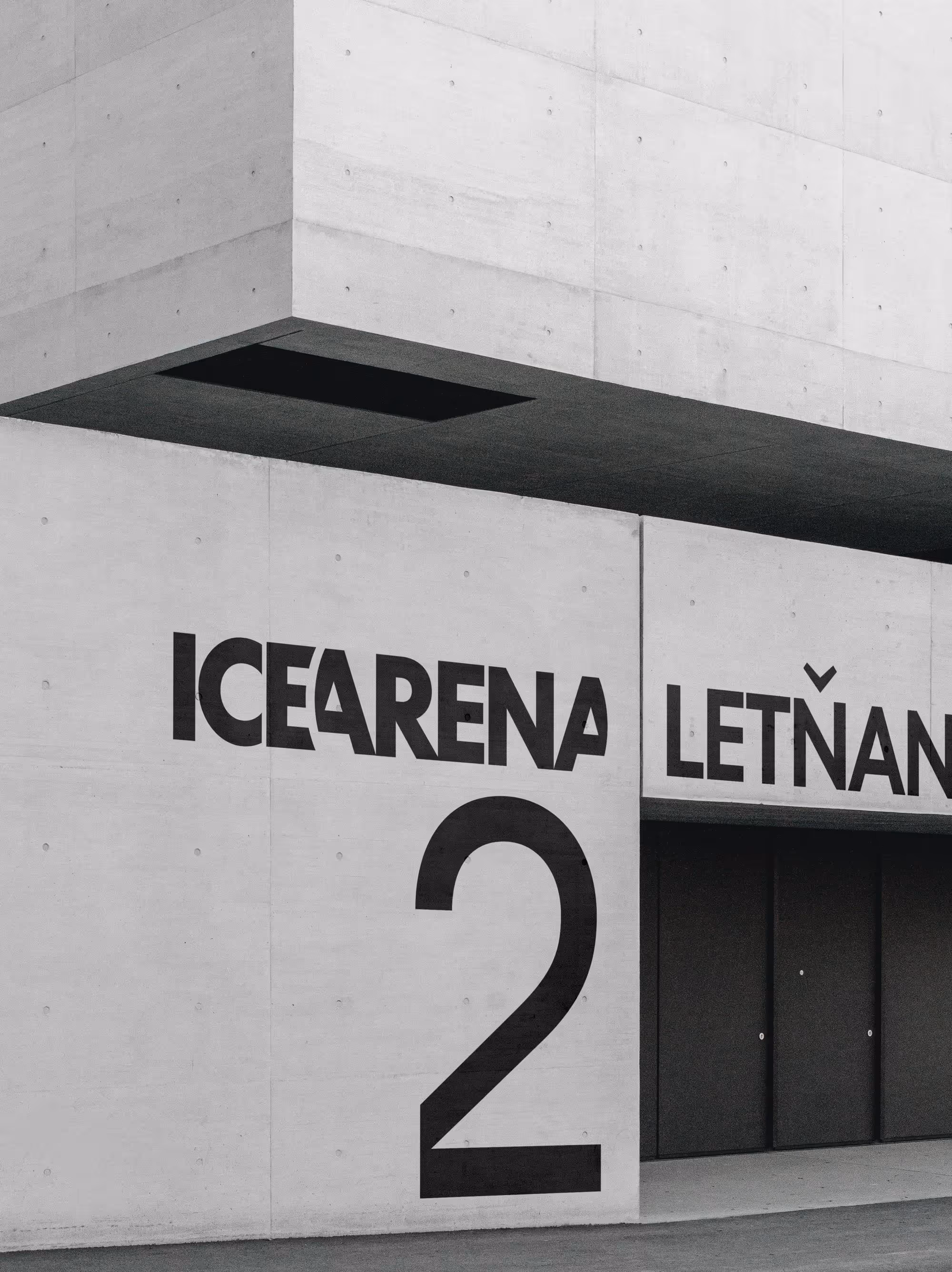 Betonová fasáda s nápisem ICE ARENA LETŇANY a číslem 2 vedle černých dveří.