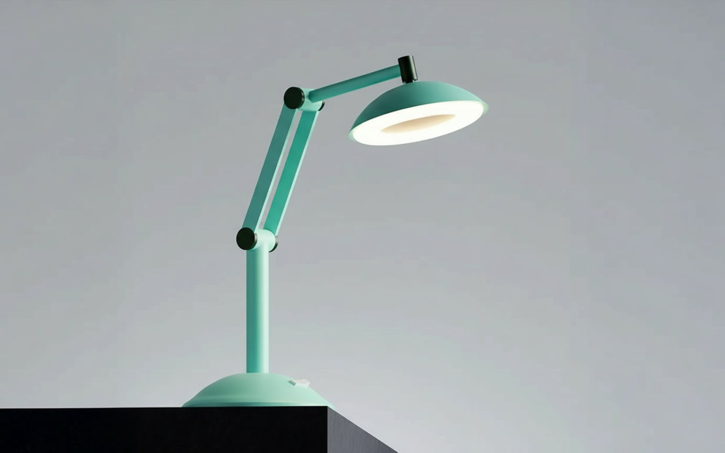 Orange adjustable desk lamp lit on the edge of a black surface with a plain gray background.