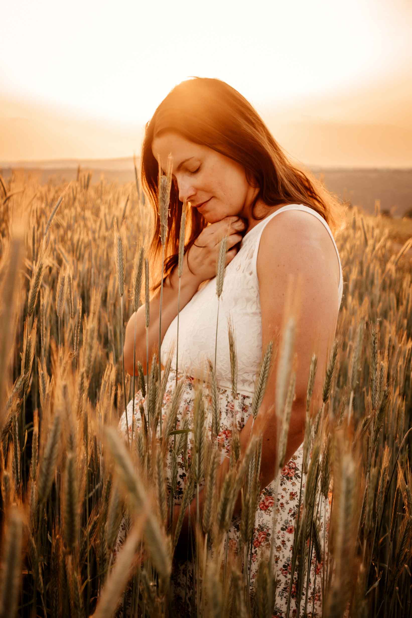 Pregnant woman in a wheat field with a sunset behind her