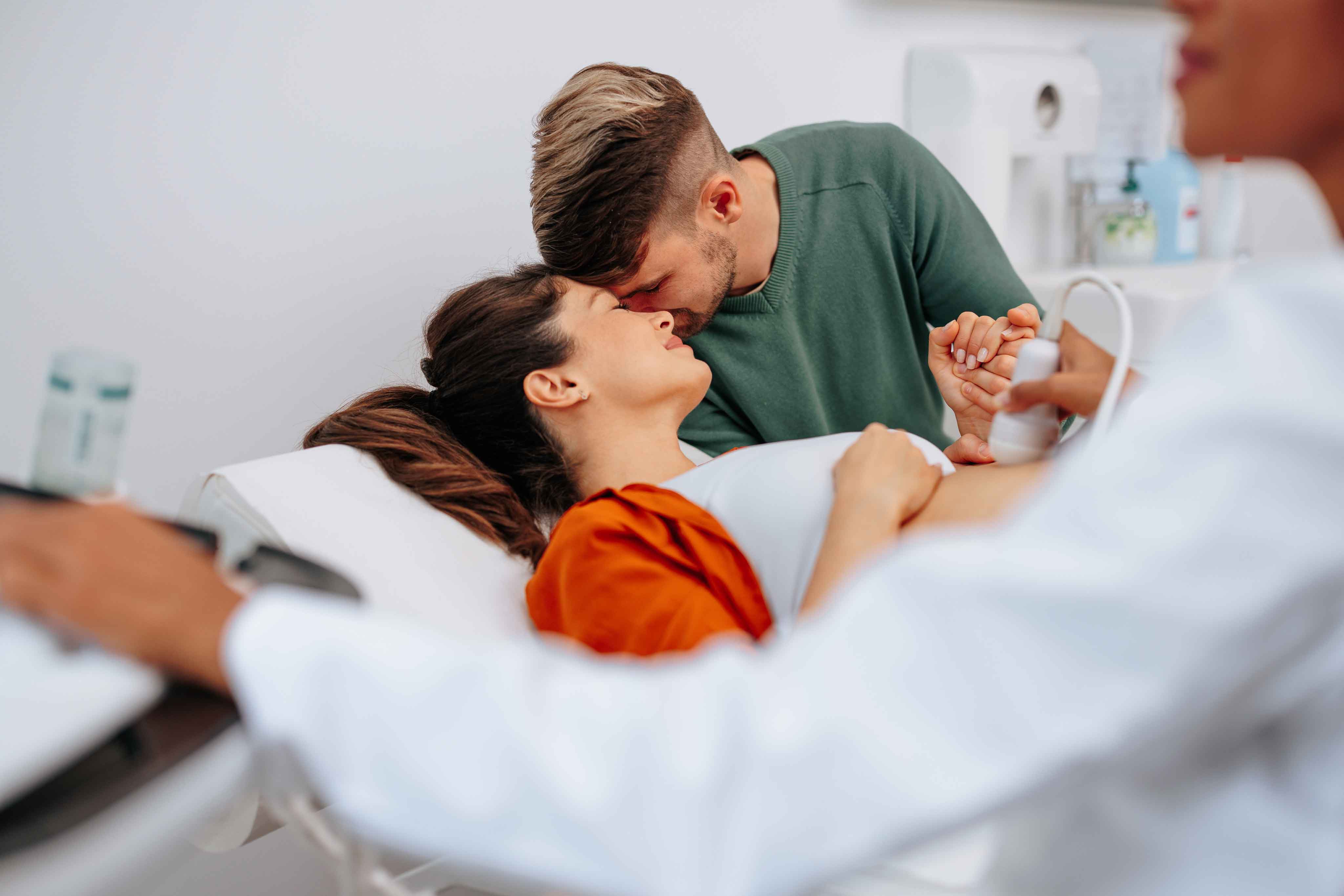A husband and wife holding each other in an emotional embrace while the woman has an ultrasound