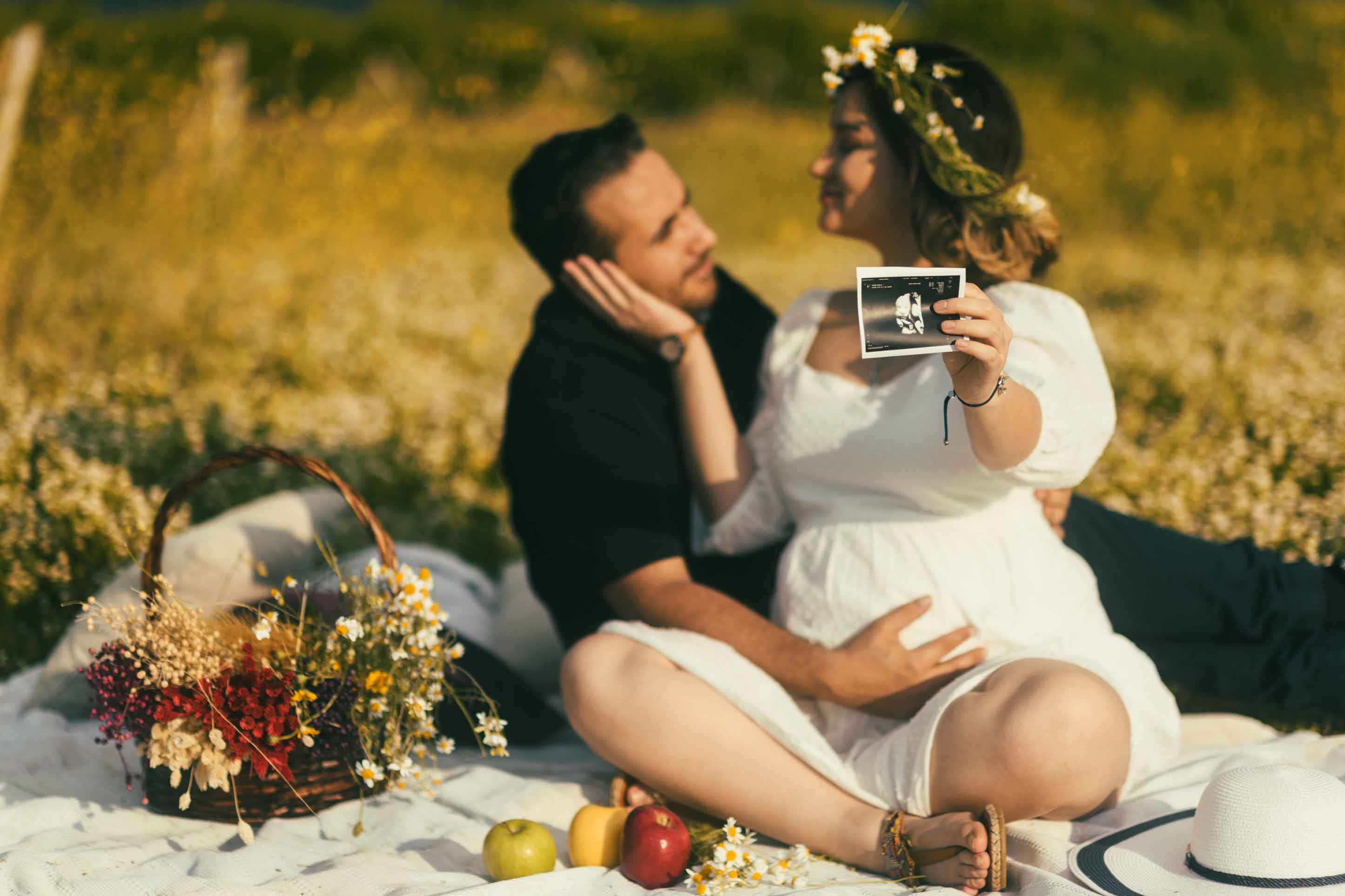 Pregnant couple at a maternity photo shoot holding their ultrasound image in a staged picnic with flowers