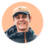Young man smiling wearing a beige cap and dark jacket with a peach background.