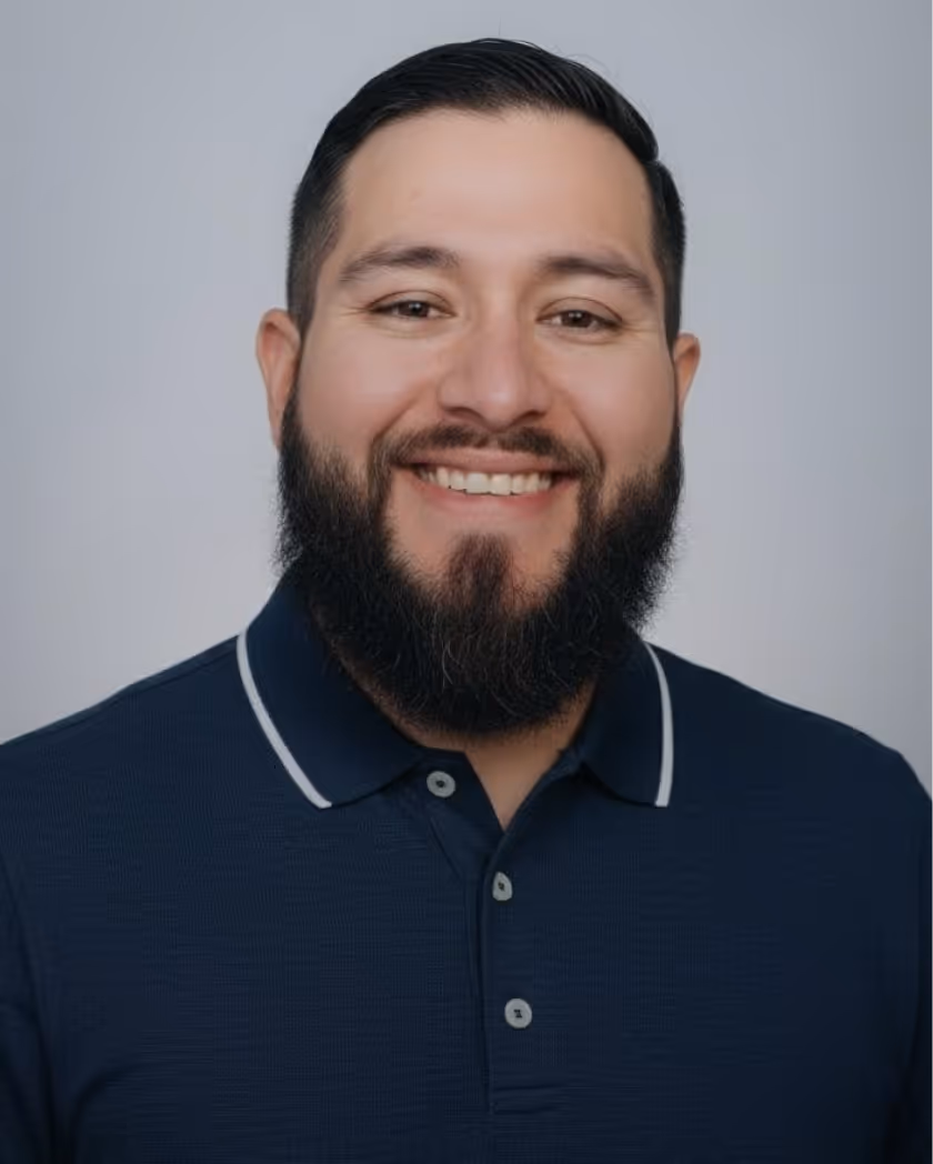 Smiling man with dark hair, beard, and mustache wearing a navy blue polo shirt with white trim on the collar.