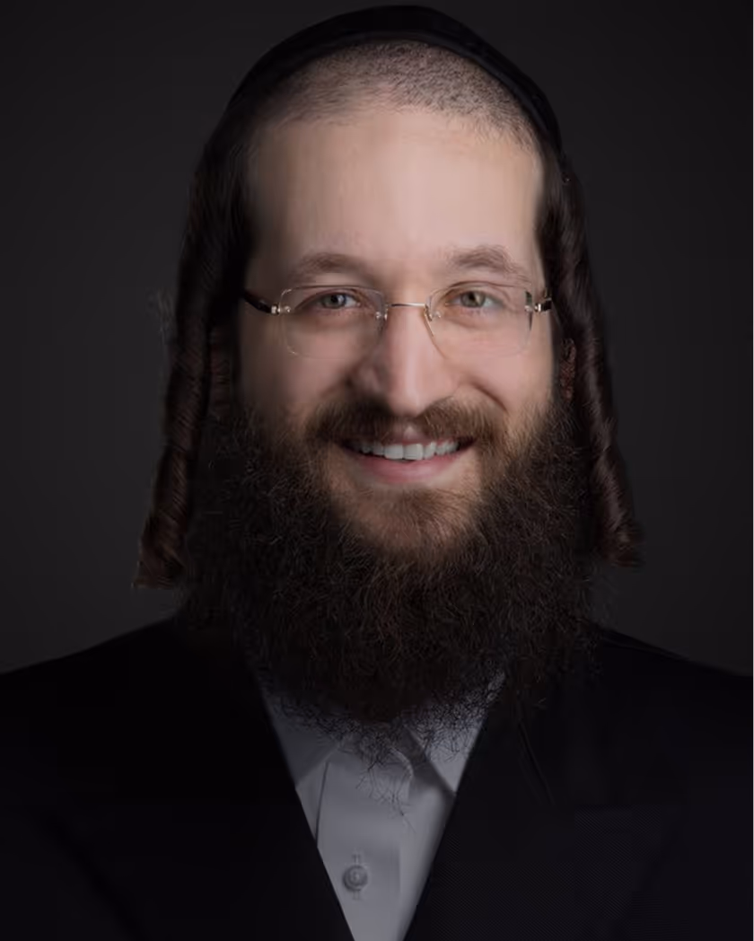 Portrait of a smiling man with glasses, a full beard, curled sidelocks, and a dark suit against a dark background.