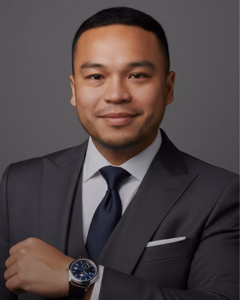 Man in dark suit, white shirt, and navy tie showing a wristwatch with a blue face.