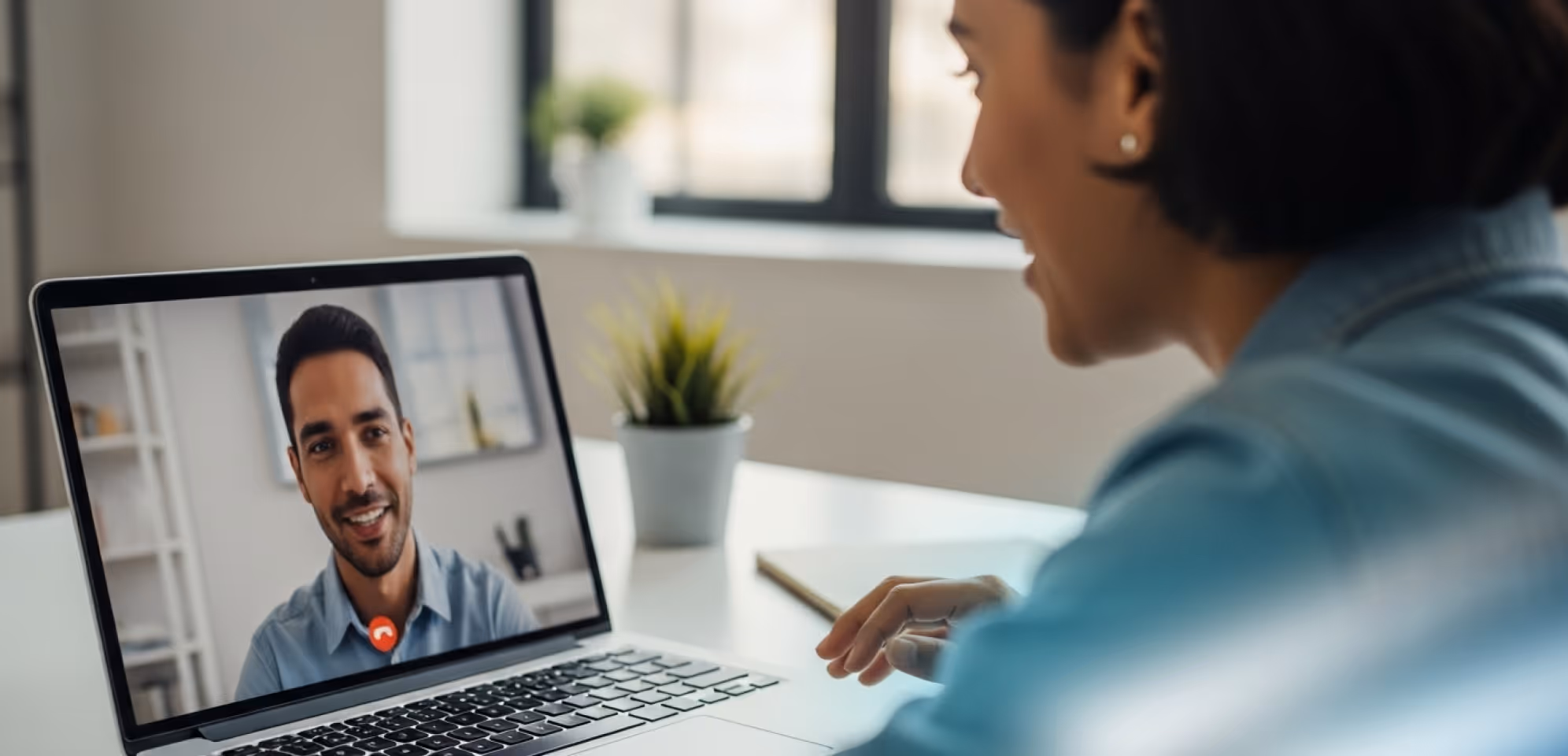 Woman engaged in a video call with a smiling man displayed on a laptop screen in a bright room.