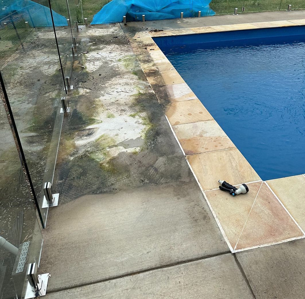 Dirty outdoor concrete surface next to a glass fence, covered in dark stains, algae, and grime buildup.