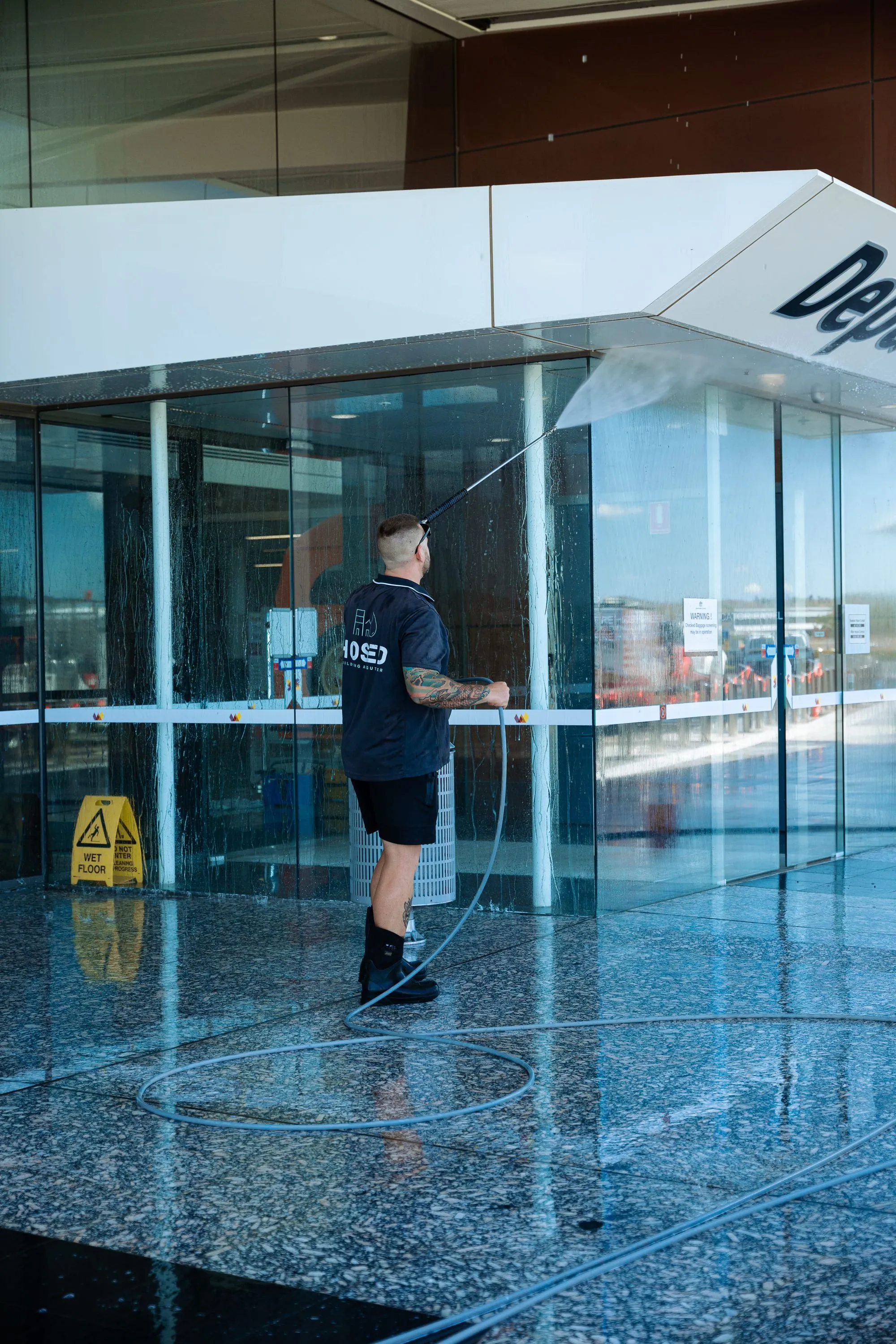Hosed Building and Gutter worker pressure washing glass entrance at airport terminal building