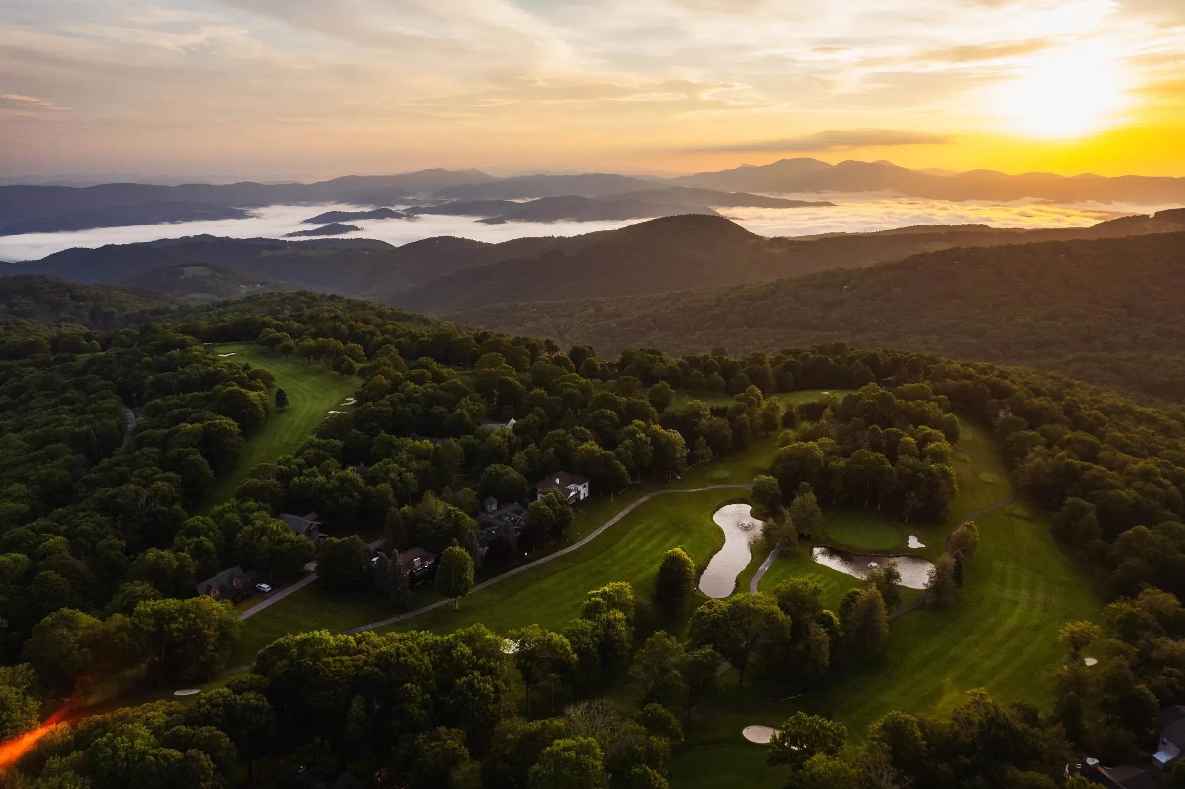 Mountain golf course and surrounding landscape photographed from the air at golden hour.