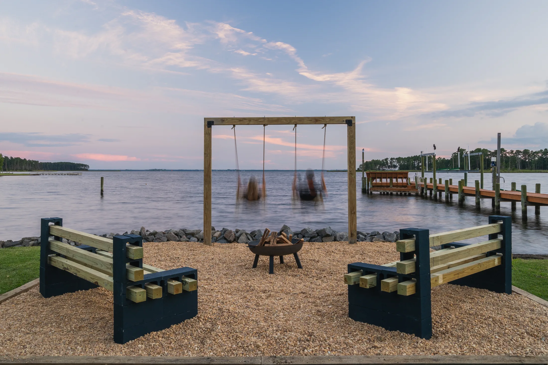 Swings and firepit beside the water at dusk