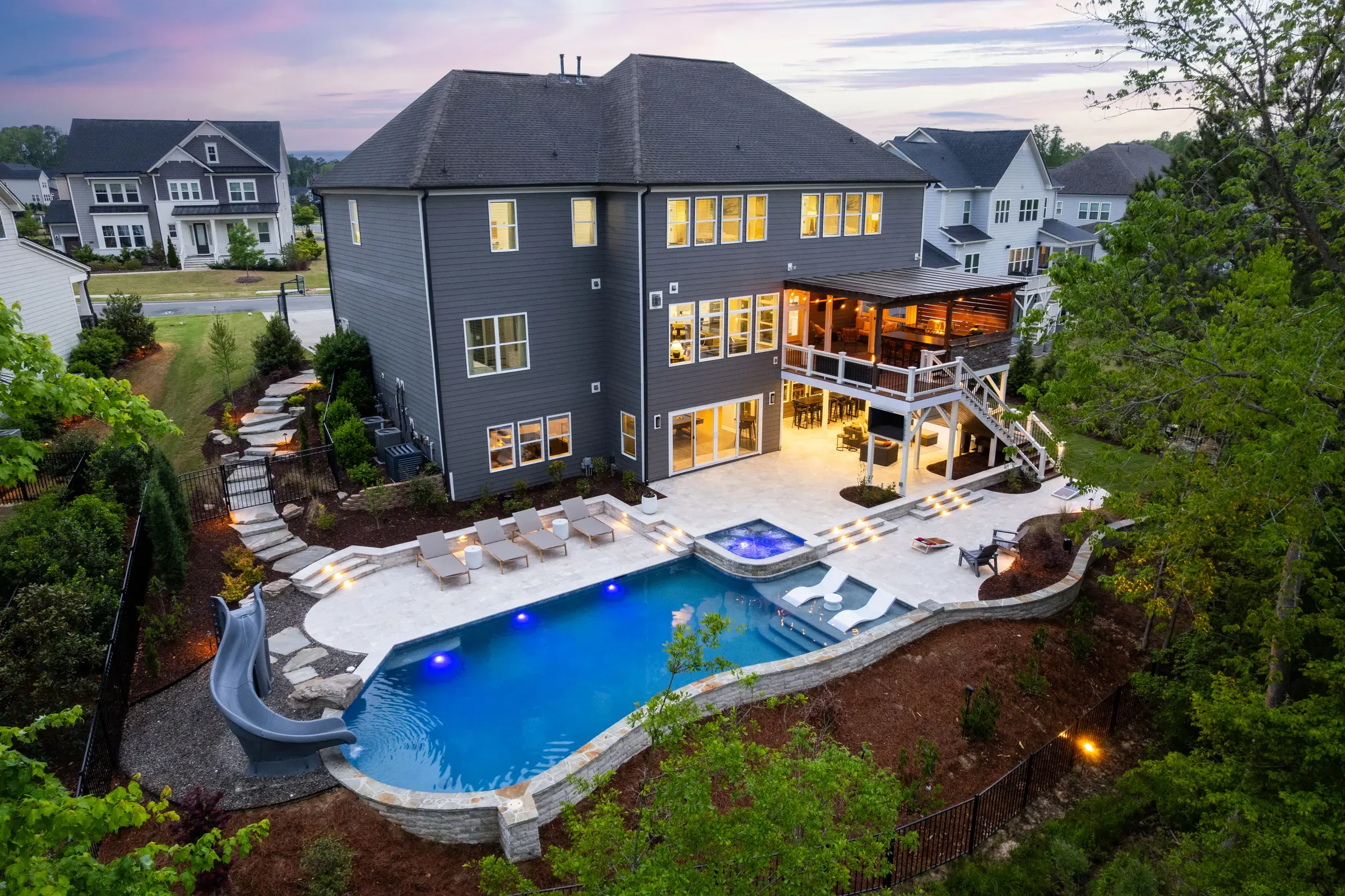 Elevated twilight view of a home with an illuminated pool, spa, and outdoor living area.
