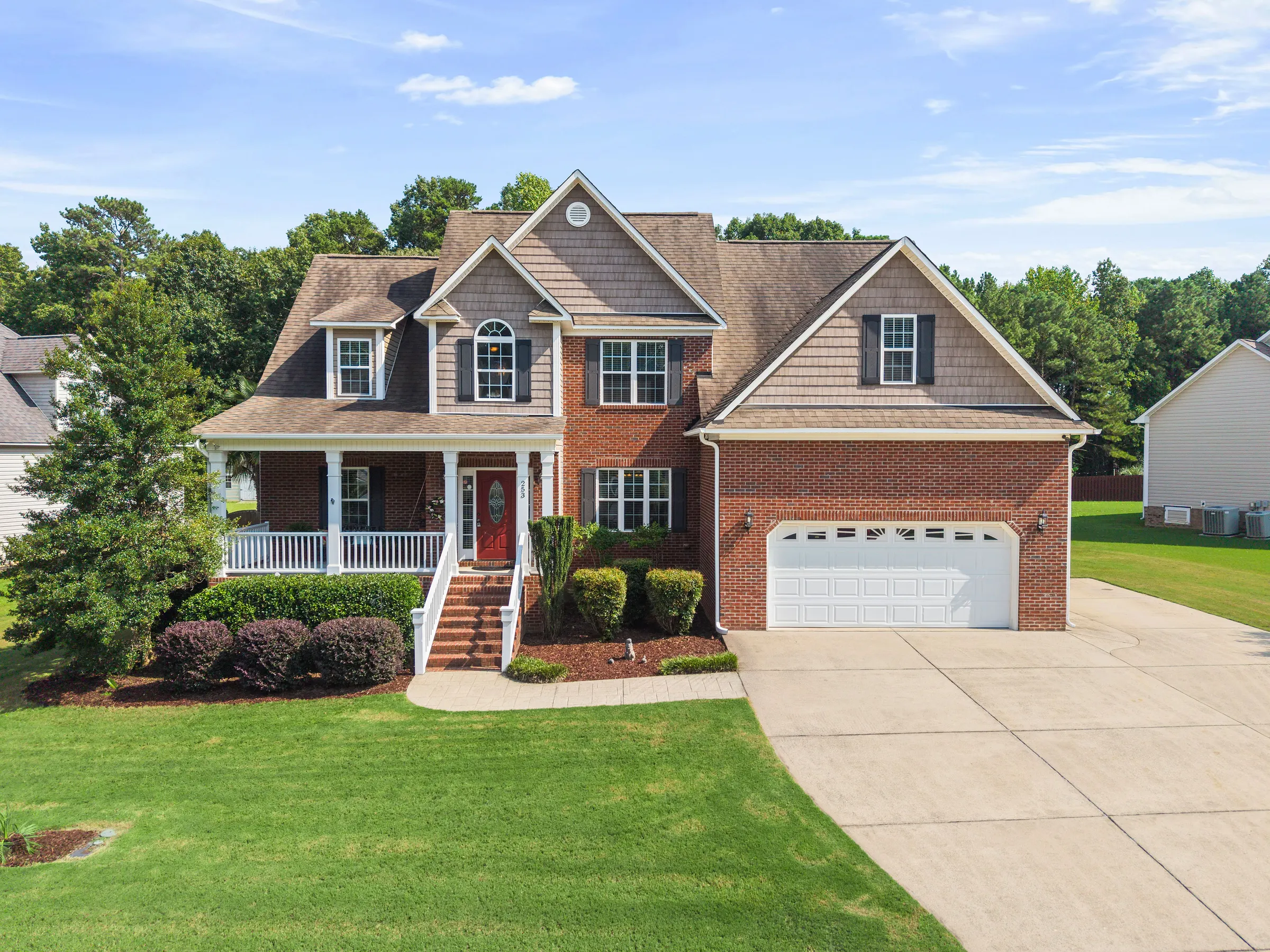 Brick and shingle home with a white front porch and green lawn in daylight.