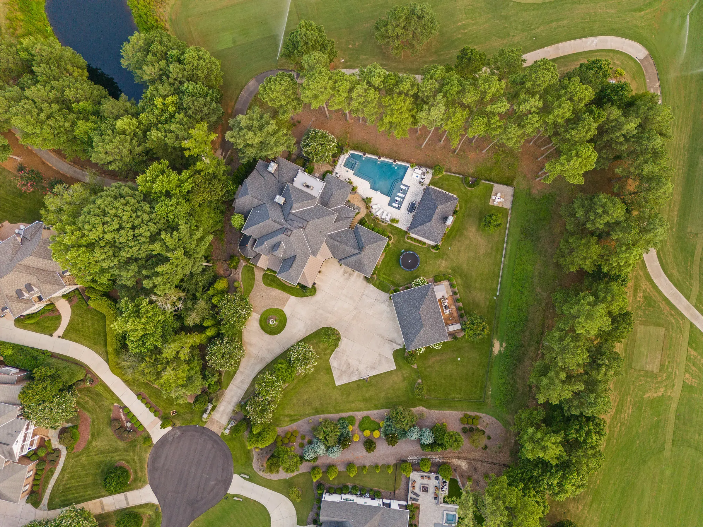 Top-down aerial view of a luxury home, swimming pool, driveway, landscaping, and surrounding golf course.