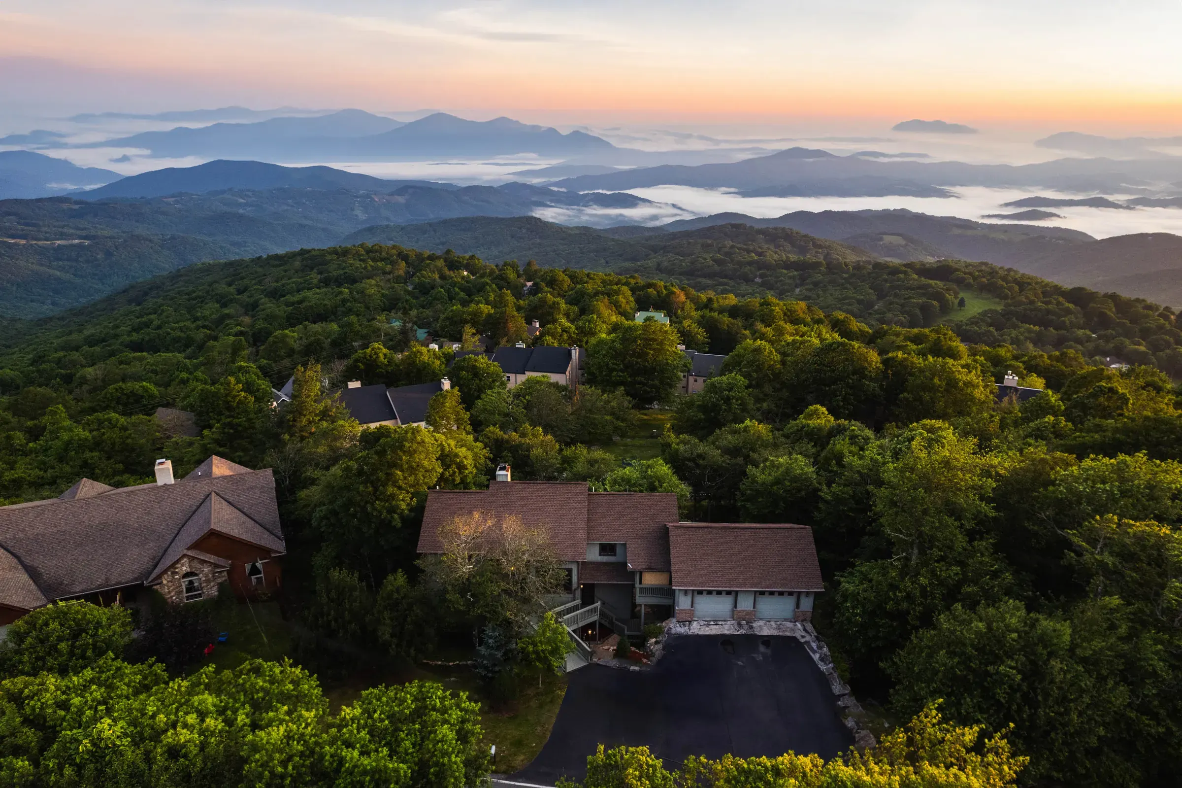 Aerial view over a mountain property with layered ridgelines and low clouds in the distance.