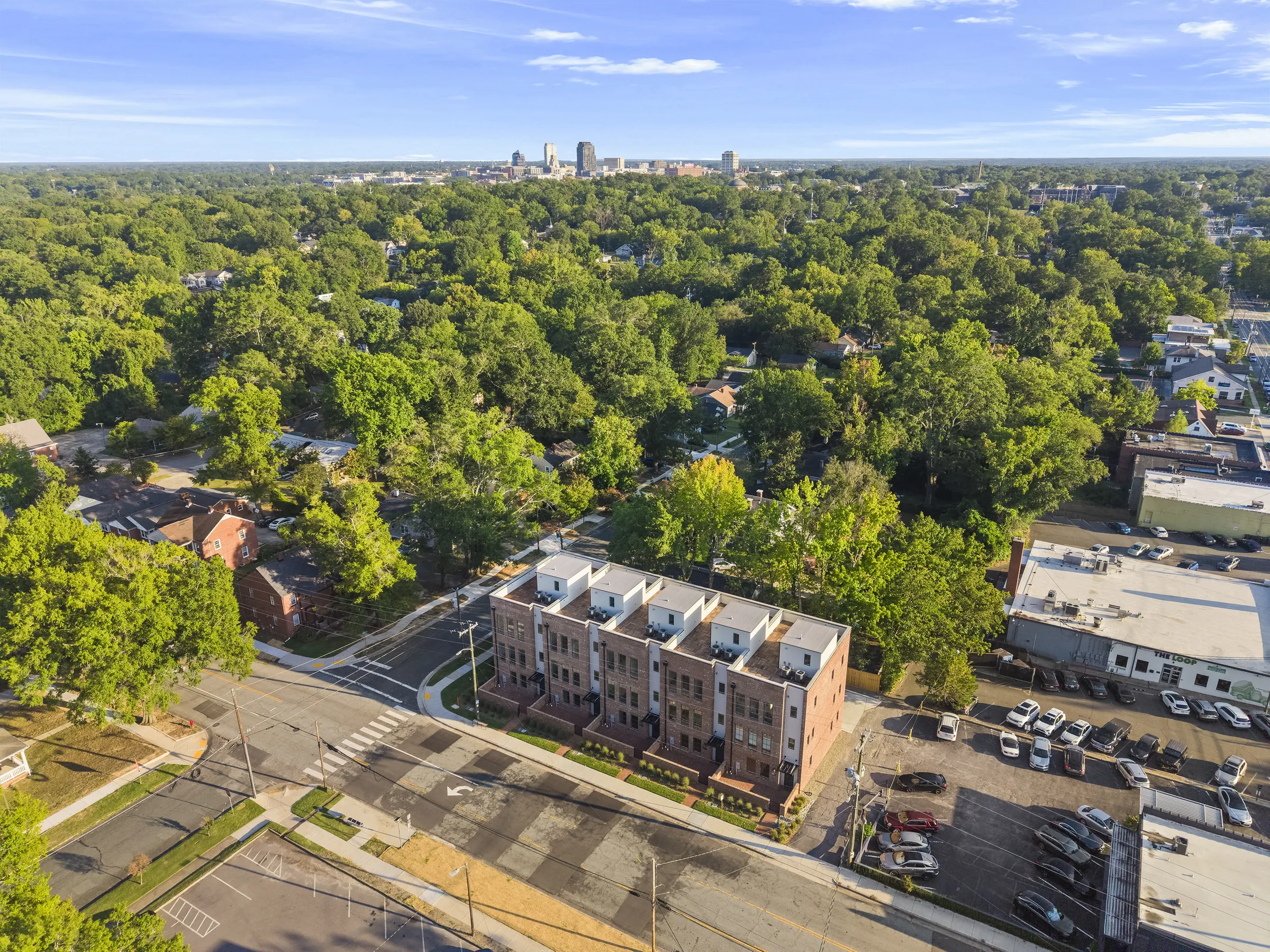 Aerial view of brick townhomes with the surrounding neighborhood and city skyline visible in the distance.