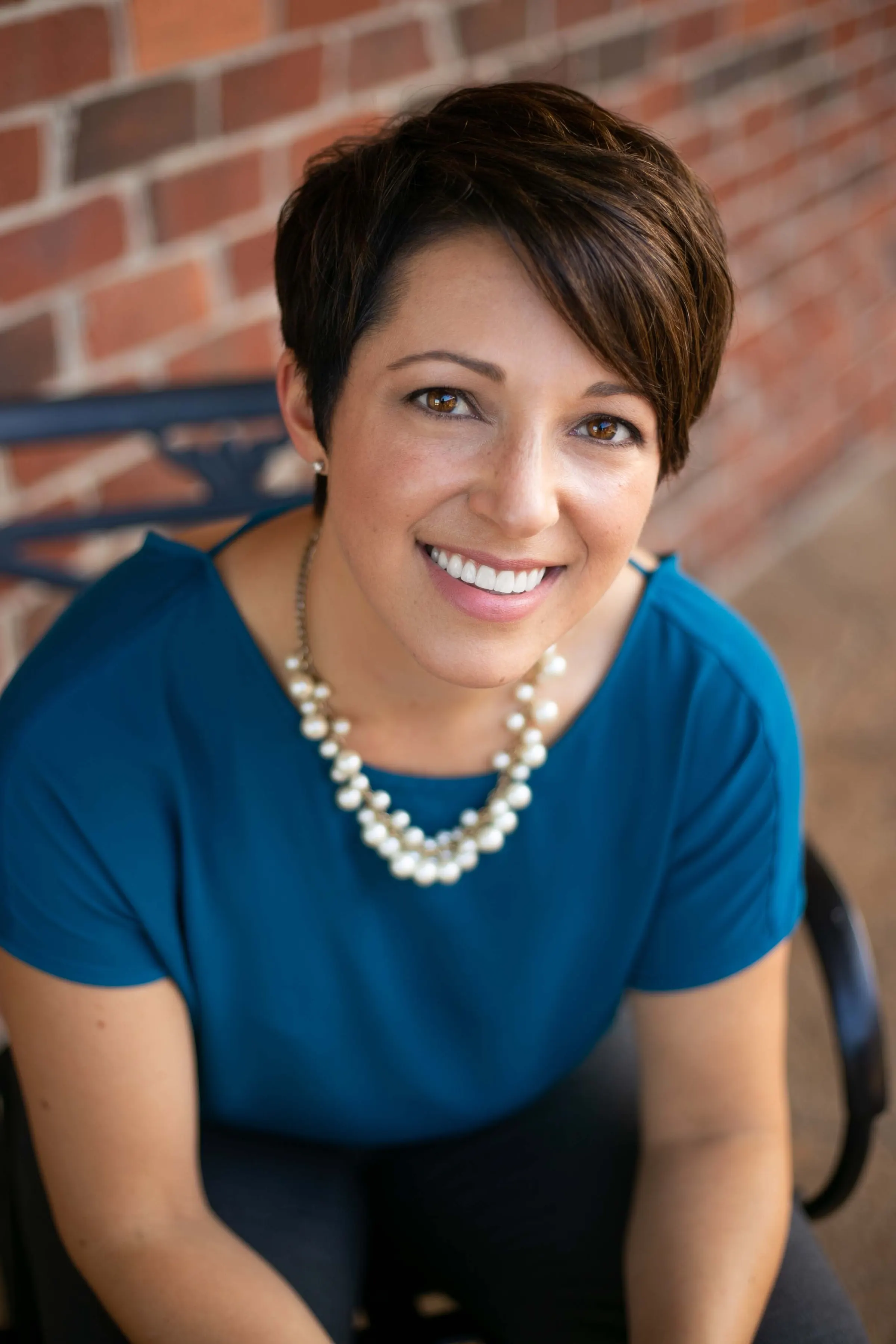 Seated headshot of a woman in a blue blouse against a brick wall