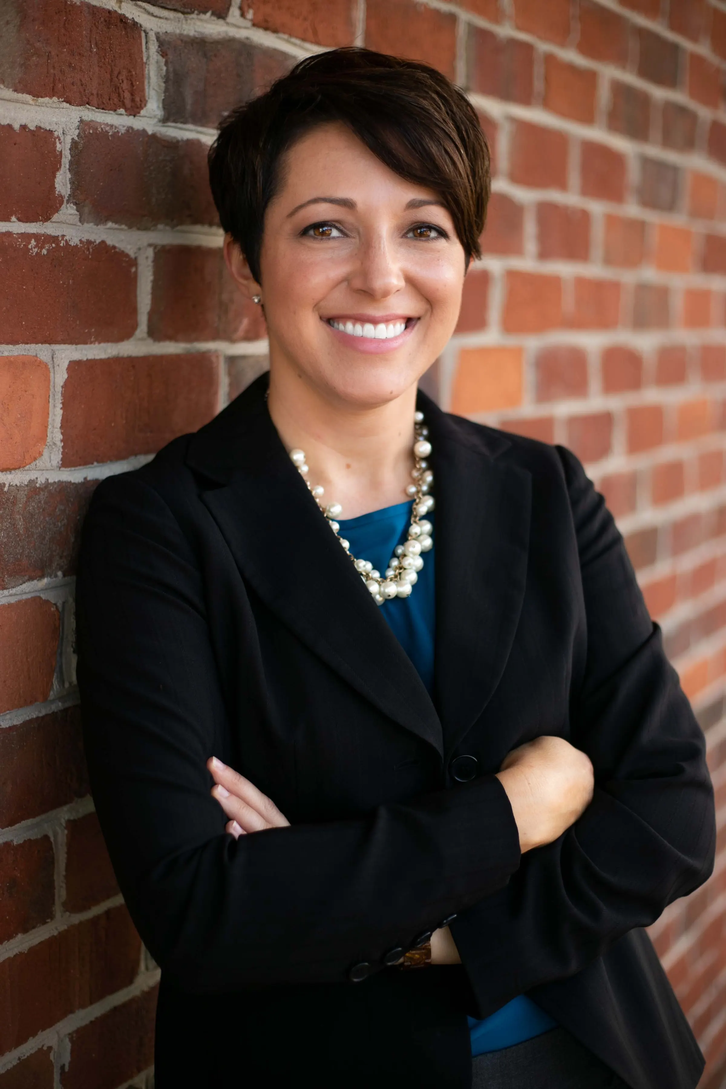 Professional portrait of a woman in a black blazer against a brick wall
