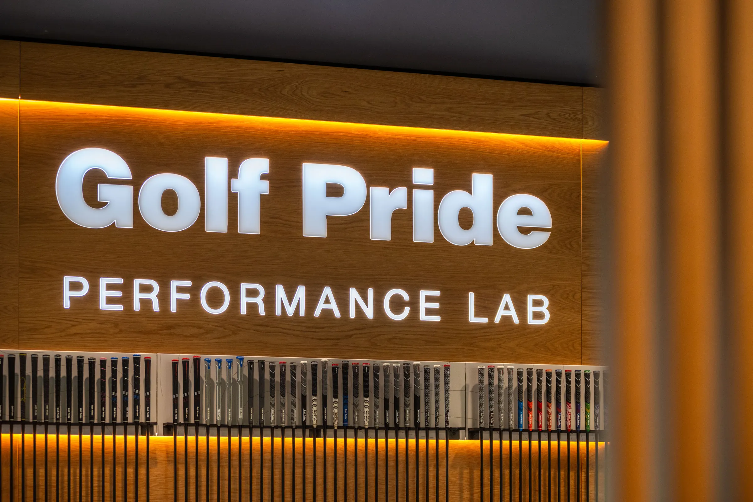 Illuminated Golf Pride Performance Lab lettering on a wood feature wall